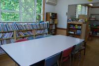 壁際にたくさん本が並べられた本棚や整理棚が設置されており、本棚の前にテーブルと椅子が置かれている七沢児童館の図書室の写真