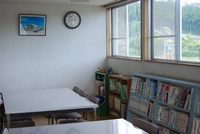壁には絵画と時計が掛けられており、窓際に本の並んだ本棚があります。本棚の前にはテーブルと椅子が並べられている下川入児童館の図書室写真