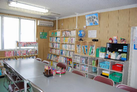 壁際の本棚に本やボックスが入っており、本棚の前にテーブルと椅子が並べられている上落合児童館の図書室の写真