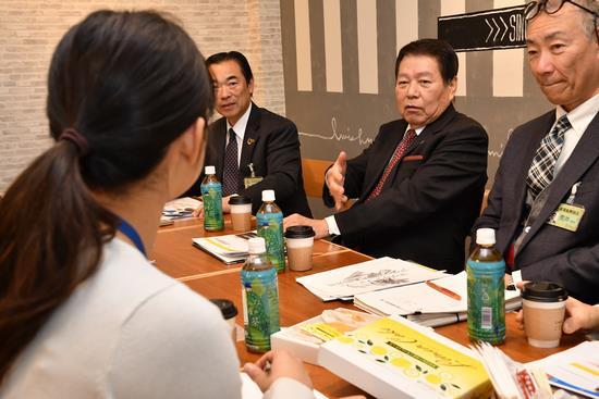 市長と関係者の男性、髪を一つにまとめて結んでいる女性と向かい合わせの席についており、意見交換の話をしている様子の写真