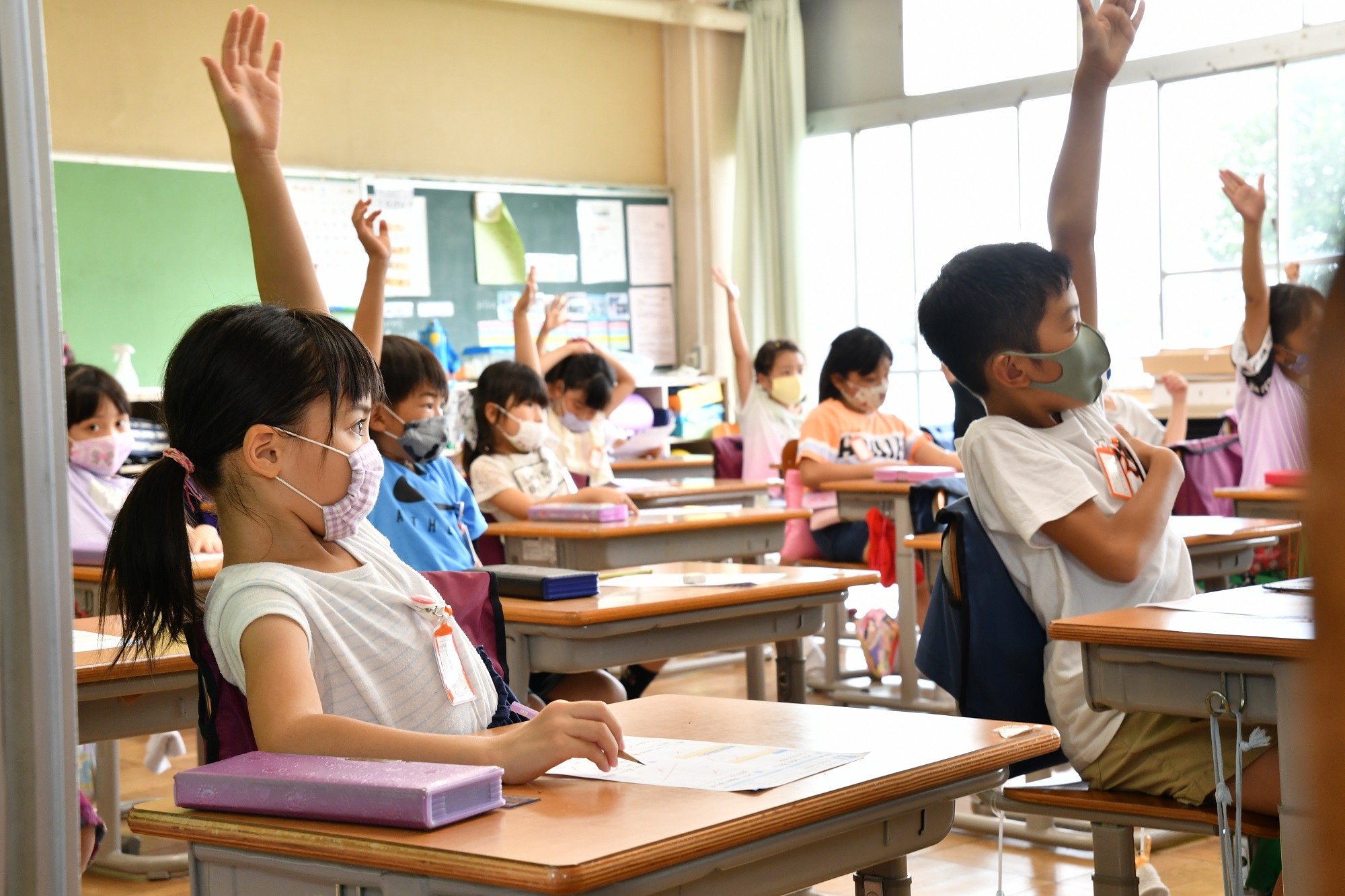 小学校の教室で子どもたちが手を挙げている様子
