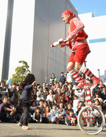 赤い衣装を着た男性が高さのある一輪車に乗っている演技を沢山の観客達が見ている写真