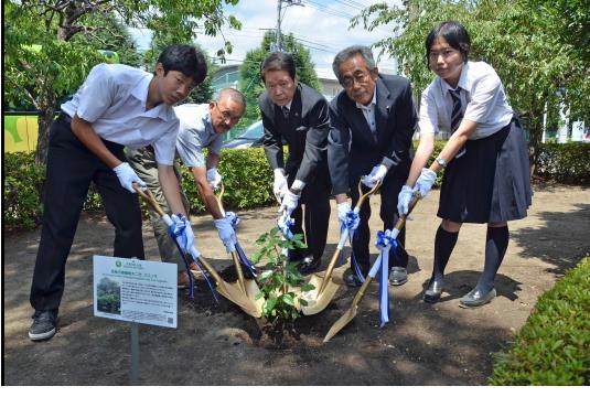 男子生徒1名、女子生徒1名、市長と関係者2名がスコップを持ちクスノキの植樹をしている写真