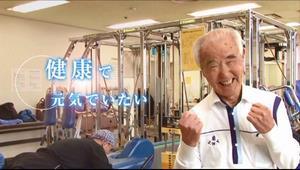 健康で元気でいたい（年配の男性がジムのトレーニング機器の前で両手でガッツポーズをして笑顔で写っている写真）
