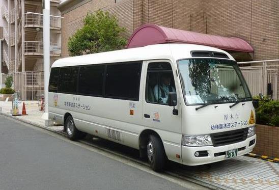 白色のバスの前方と横に「幼稚園送迎ステーション」と書かれている送迎バスを斜めから撮影した写真