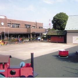 園庭に赤い汽車の乗り物や赤い花の遊具があり、奥に茶色い建物の厚南幼児園の写真