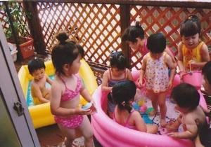 黄色とピンク色のビニールプールに水着を着て遊んでいる、たんぽぽコミュニティの園児たちの写真