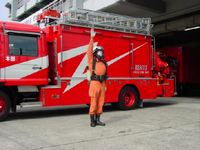 1名のオレンジ色の服を着た隊員が消防自動車の前に立ち右手をあげている写真