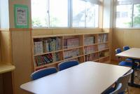 窓際にたくさんの本が並べられた本棚があり、本棚の前にテーブルと椅子が設置してある愛甲児童館の図書室の写真
