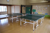 壁には色画用紙や折り紙で作成されたものが飾られており、フローリングには卓球台が2台設置してある遊戯室と隣に和室がある妻田児童館館内の写真