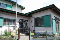 入口にある金網の柵からプランターの花々が見えている緑色のひまわり児童館の正面写真