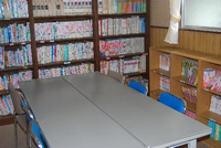 壁際にたくさん本が並べられた本棚が設置され、本棚の前にテーブルと椅子がある館内（図書室）の写真