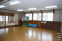 窓際の壁側に黒板や遊具の入ったかご、棚が設置されており、隣には畳の部屋がある厚木南児童館の遊戯室の写真