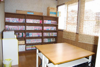 壁際にたくさん本が並べられた本棚が設置され、本棚の前にテーブルと椅子があり、窓には簾がかけられている厚木南児童館の図書室の写真