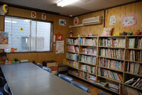 壁際に設置してある棚にたくさんの本が並べてあります。棚の前には椅子とテーブルがある中戸田児童館の図書室の写真