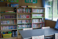 壁際にたくさんの本が並んだ本棚があり、本棚の前にテーブルと椅子があるまつかげ台児童館の図書室の写真