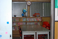 窓際にたくさん本が並べられた本棚が設置され、本棚の前にテーブルと椅子がある館内（図書室）の写真