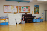 飾りつけのされた掲示板やフラフープ、おもちゃやピアノが置かれた山際児童館内遊戯室の写真