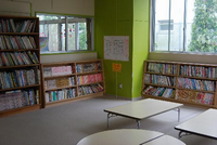 壁に本棚が設置され、沢山の本が並んでおり中央には机が設置されている館内（図書室）の写真