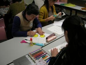 参加者の女性が色塗りをしたり、ハサミで紙を切っている手遊び講習会の様子