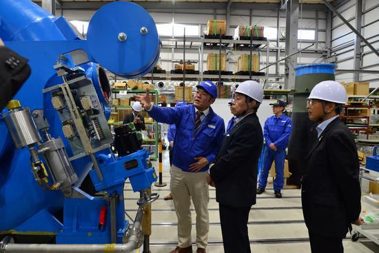 青色で大きな電動水車の機械の前で、田中水力株式会社の方から市長が機械の説明をが受けている様子の写真