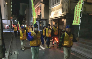 黄色いベストを着て、防犯旗を持ち、繁華街をパトロールしている方々の写真