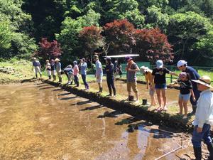 水が張られた田んぼのふちに一列に並んで立っている七沢里山づくりの会会員の写真