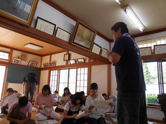 取り組みについて話をしている小山田さんと資料を見ながら説明を聞いているツアー参加者の写真