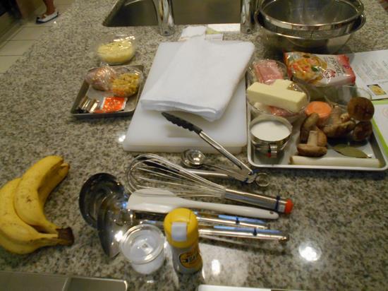 テーブルに置かれたバナナや牛乳、椎茸、マカロニなどの食材と、お玉や泡だて器などの道具の写真