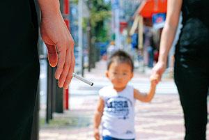 歩道で手を繋いで歩いている子供とすれ違う人が火の付いたたばこを持っている写真