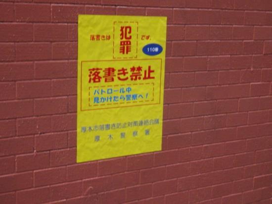 レンガ調の茶色の壁に黄色い「落書き禁止ステッカー」が貼られている写真