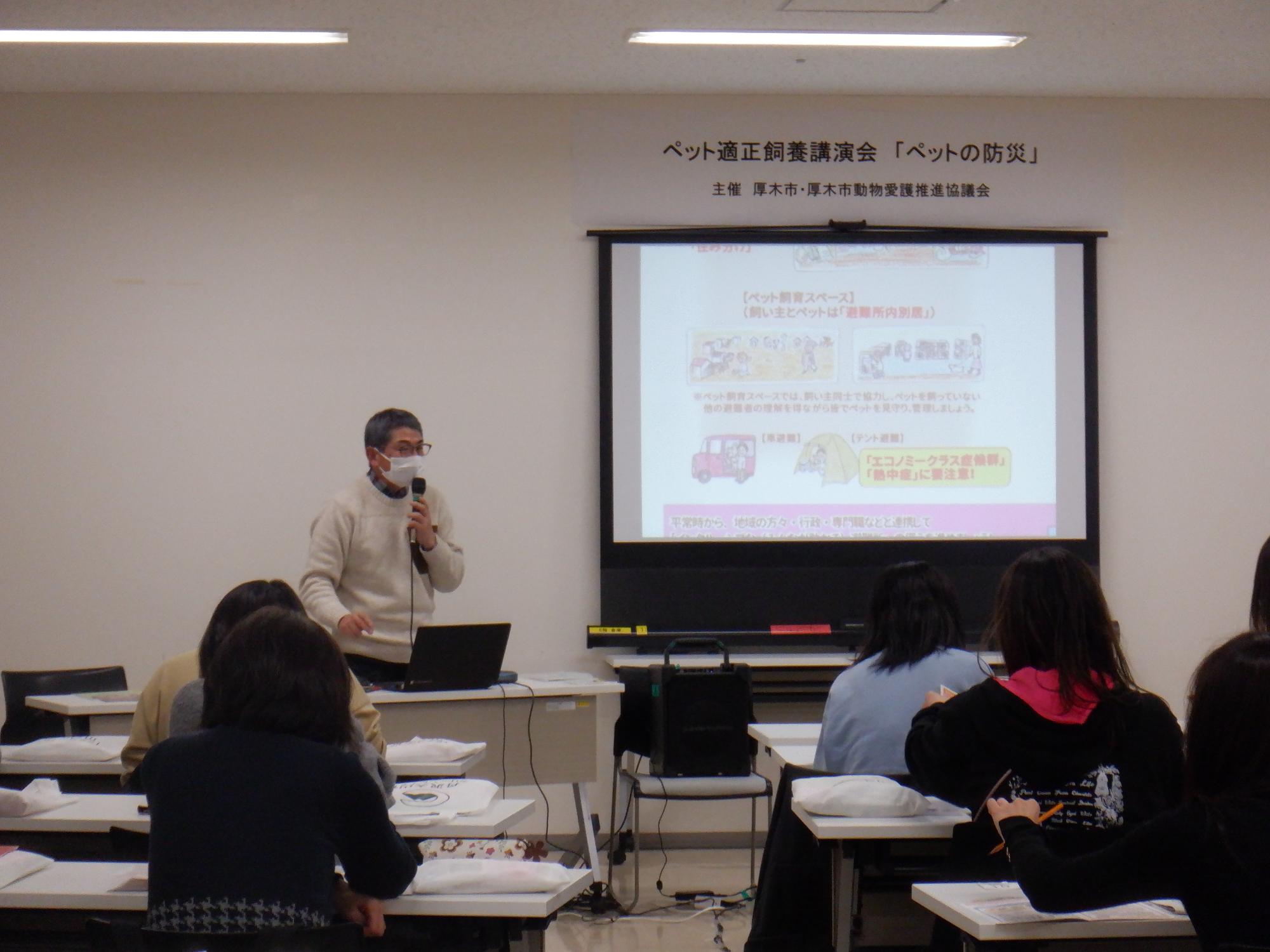 参加者の前でマイクを持って講演する倉島勝治先生の写真