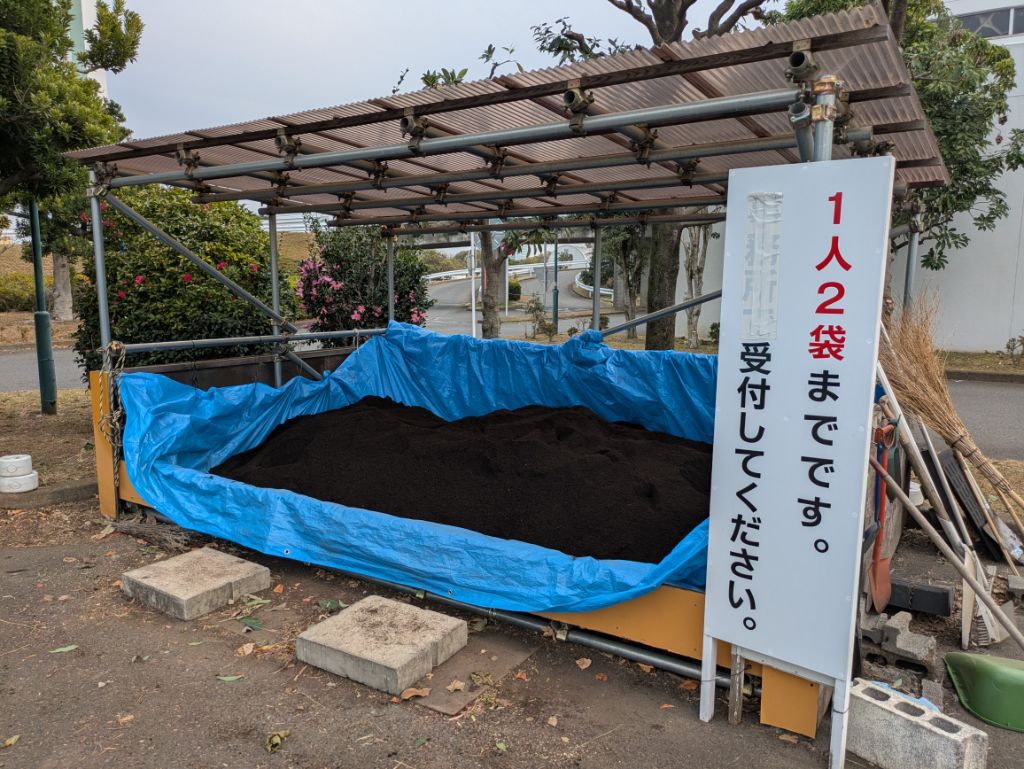青いビニールシートの上に堆肥が置かれて脇に案内の立て看板が置かれている堆肥配布場所の写真