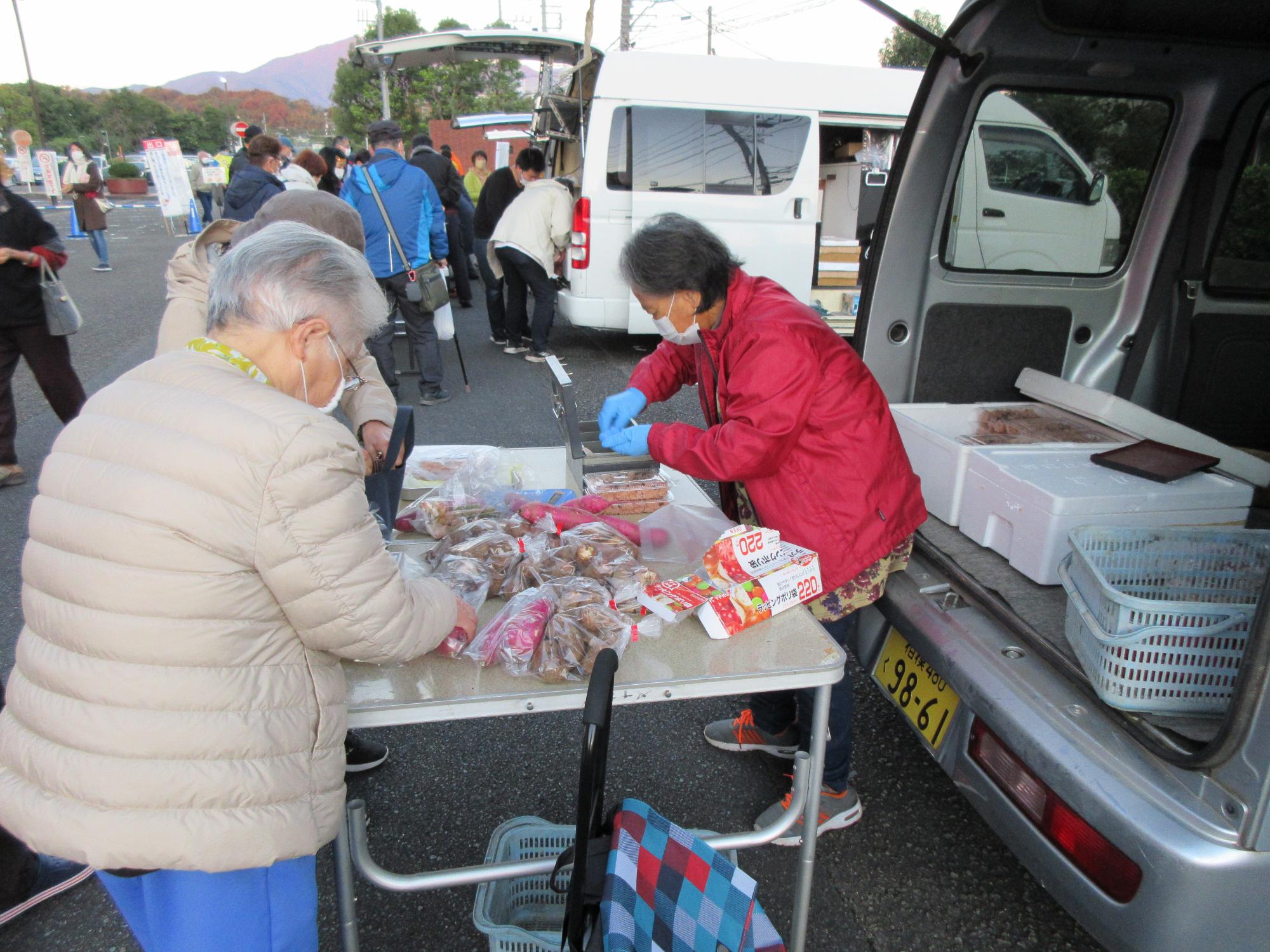 テーブルの上に並べられた商品を見ている人と店の女性