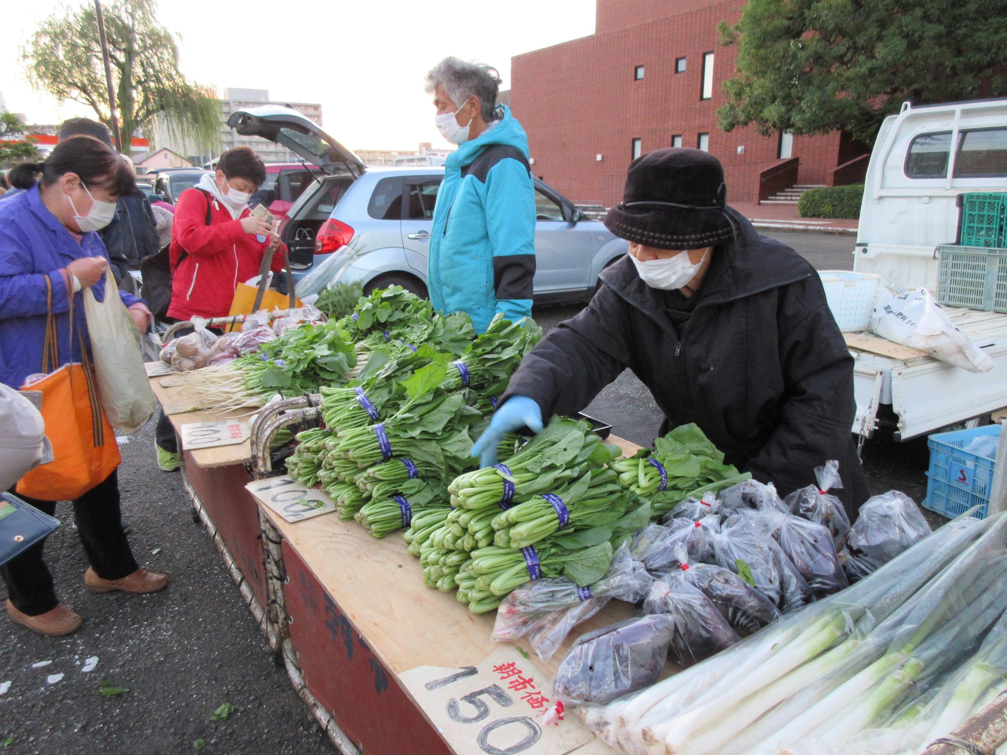 ネギやナスなどの野菜が並べられている台を見ている人の写真