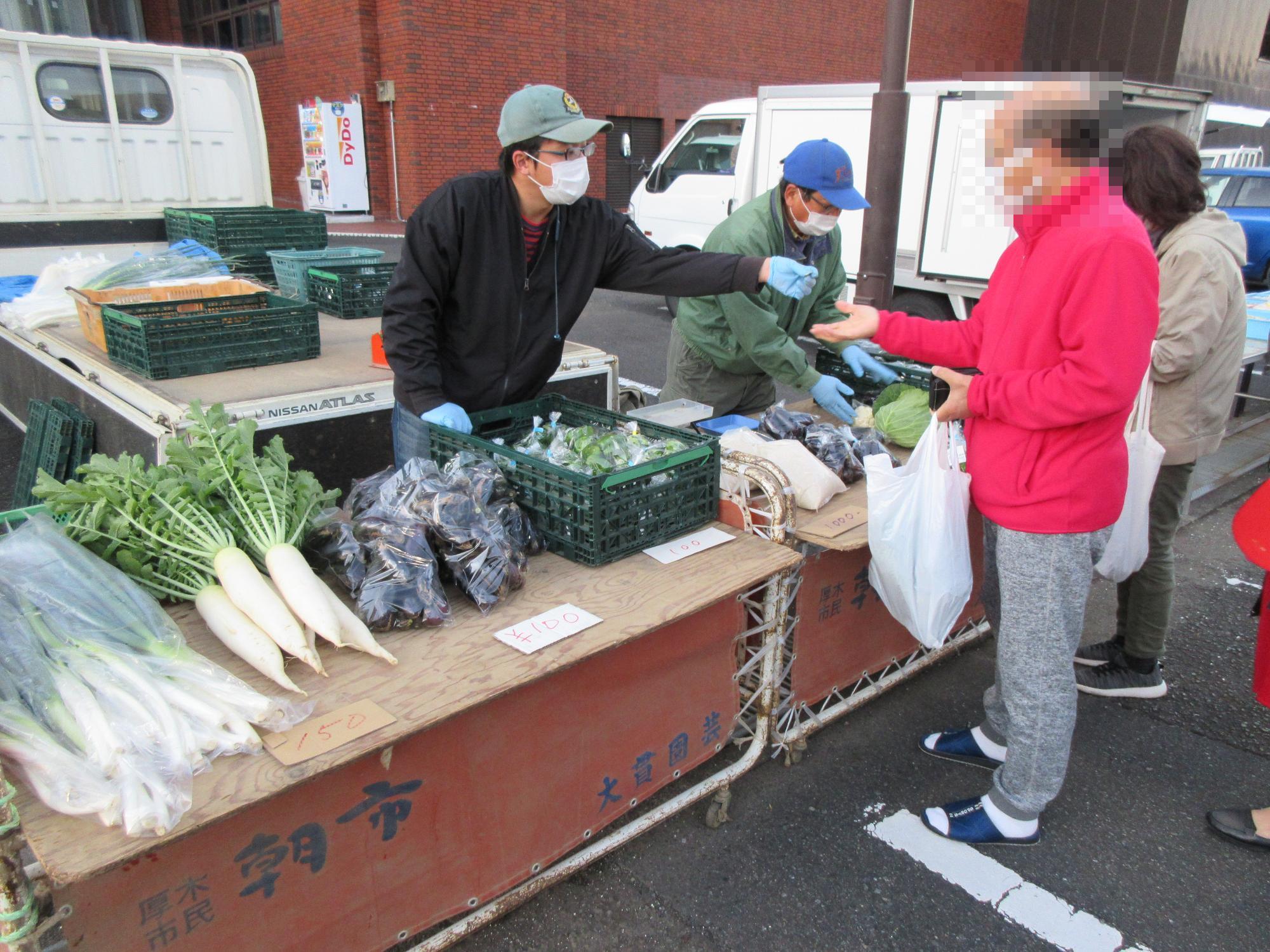 台に並べられた野菜と野菜を販売する人の写真