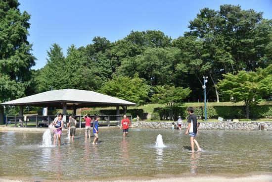 青空の下ぼうさいの丘公園の親水広場で水遊びを楽しむ子供たちの写真