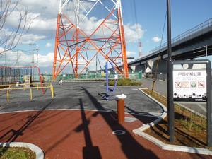 右側に高速道路が通る下に、大きなタワーが立っており手前に水飲み場やブランコが設置されている戸田小柳公園の写真