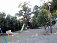 公園の周りに木々が生い茂っており、滑り台などが設置している北ヶ谷公園の写真