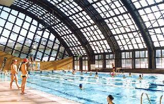 天井と横側が格子状になっていて日差しが入って明るい屋内のプールで泳いでいる人たちの写真