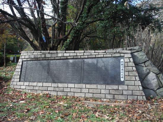大きな木の手前に石枠の中に黒地に文字が書かれてある、四季の森記念碑の写真