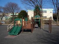 小学校に隣接している公園に設置されている、緑や茶色で統一されてすべり台や雲梯などがある複合遊具の写真