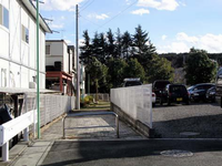 左側に2階建てのプレハブが建ち並び、右側には駐車場のある間の細い通路を入って行った先の奥にベンチが設置されている八ツ橋公園の写真