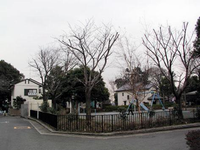黒色の低い柵で囲まれている園内周囲には樹木が点在しており、左奥に鉄棒、右側にすべり台やブランコなどの遊具が設置されている、くすのき公園の写真