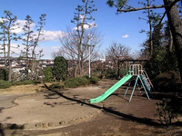高台にある園内周囲には樹木が点在しており、右側にすべり台が設置されている曽野公園の写真