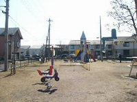 周囲に集合住宅が並んでいる一角にある園内奥に、三角屋根のロケットの形をした複合遊具、手前に赤色と紫色のスプリング遊具などが設置されている勝見公園の写真