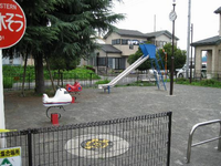 園内左側にある大きな木の右側にすべり台、手前に飛行機の形をしたスプリング遊具が設置されている公園の写真