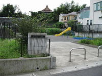 黒色のフェンスで囲まれた住宅街の一角にあり、黄色のすべり台や鉄棒などの遊具が設置されている、ぐみだ公園の写真