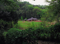 周囲を森に囲まれ開けた広い敷地の奥に、三角屋根の平屋建ての建物が建っている七沢森林公園の写真