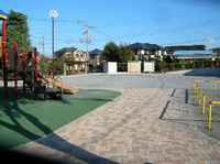 住宅街の一角にある園内奥には広場があり、手前左に複合遊具がある写真